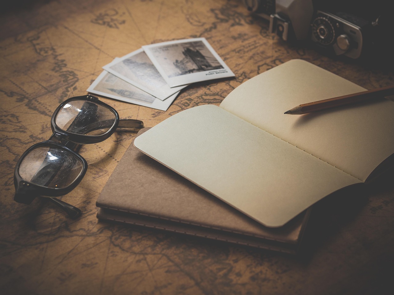 Cuaderno abierto, gafas y fotografías antiguas sobre un mapa